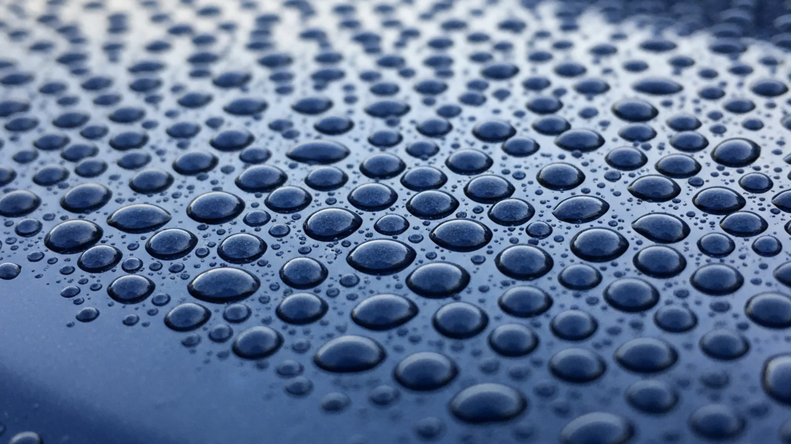 Water droplets beading on a ceramic-coated deep blue car surface